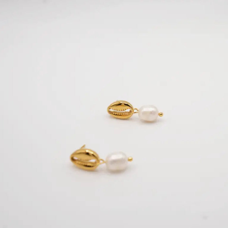 Pair of gold cowries and pearl earrings on a light gray background