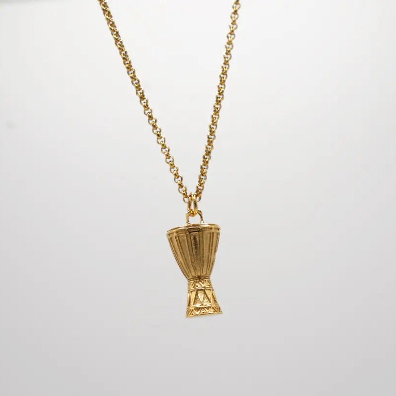 Gold necklace with a unique  Djembe pendant on a light gray background. African drum necklace 