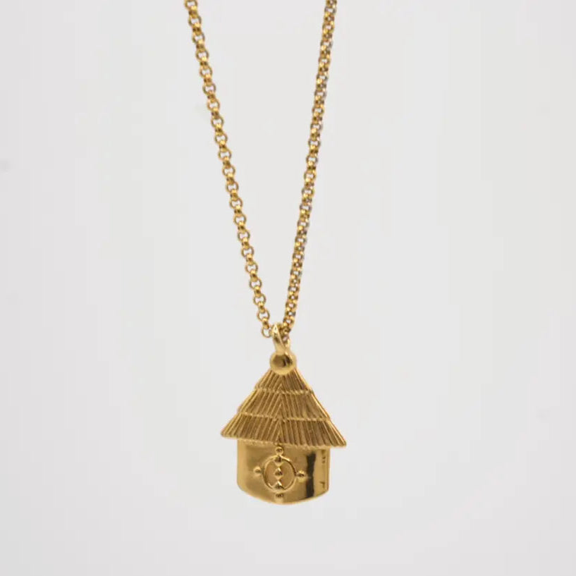 Gold necklace with an African hut pendant on a light gray background