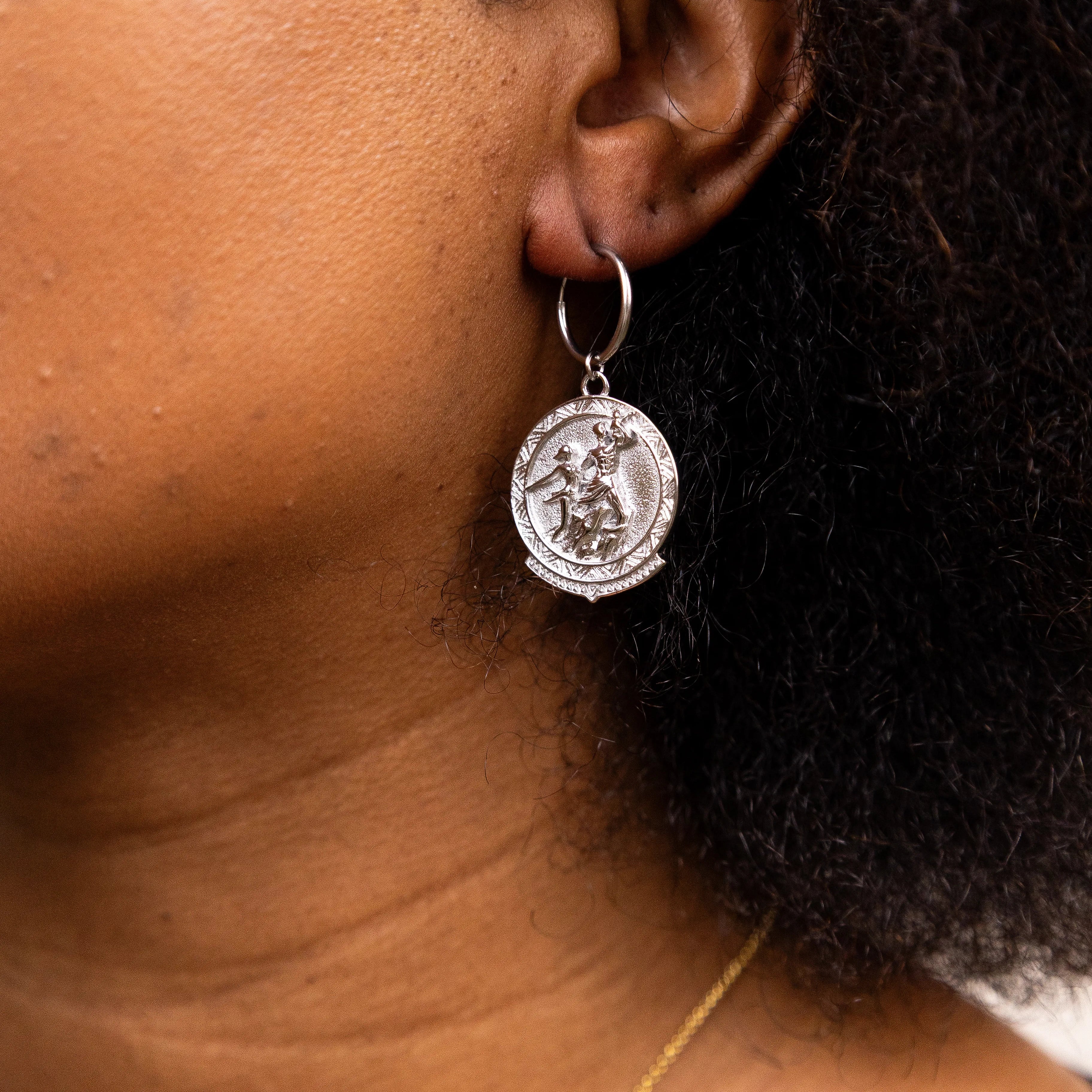 Close-up of a person wearing a silver coin earring with the Senegal renaissance monument design.