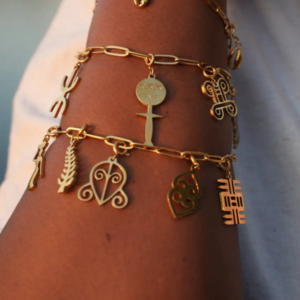 Gold bracelet with various african and adinkra charms on a wrist against a neutral background