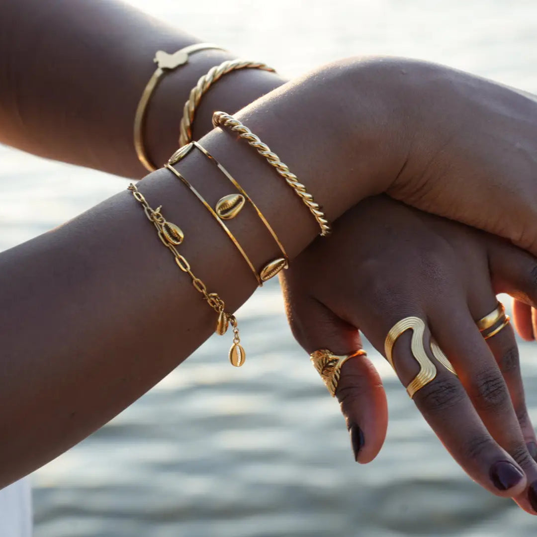 Close-up of hands with gold jewelry against a blurred water background