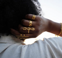 Hand wearing multiple gold african rings from the jewelry brand Doore Dasi with a blurred background