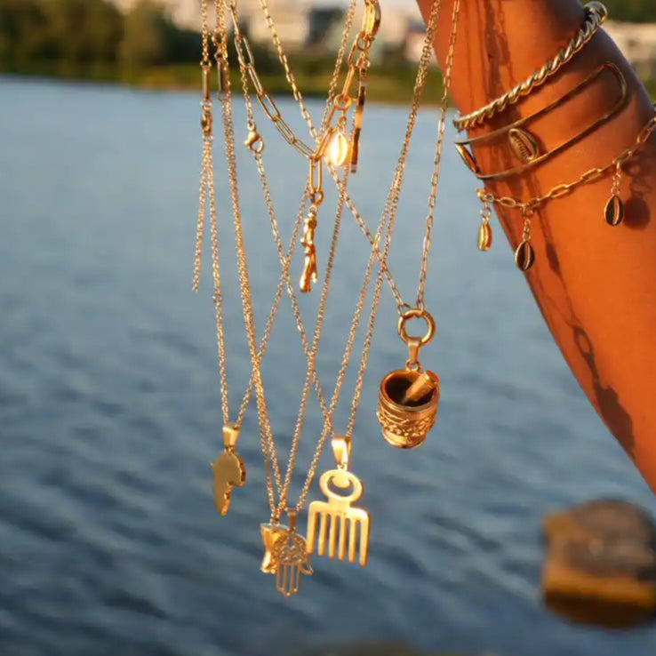 Hand holding gold necklaces with various pendants by a body of water.