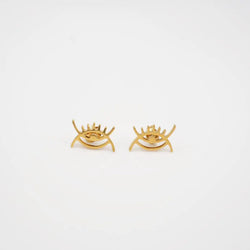 Gold eye-shaped earrings on a light gray background from adinkra symbols 