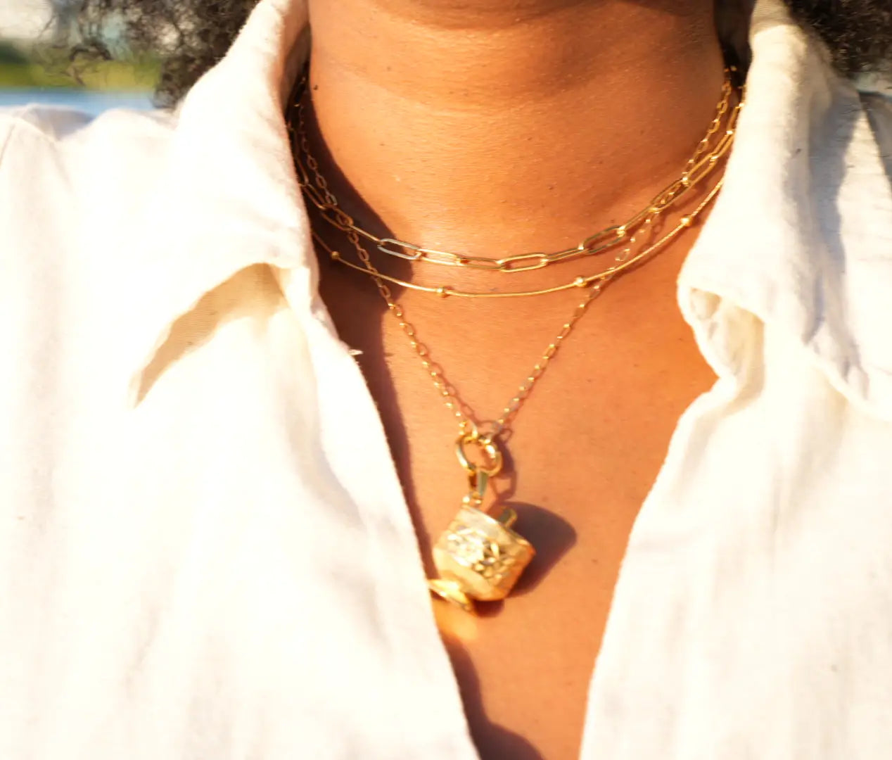 Close-up of a person wearing gold necklaces with a blurred outdoor background
