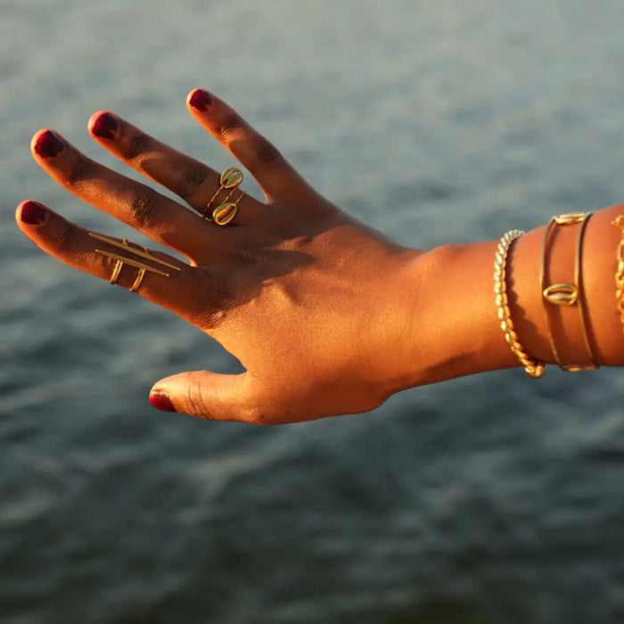 Hand with gold rings and bracelets against a blurred water background